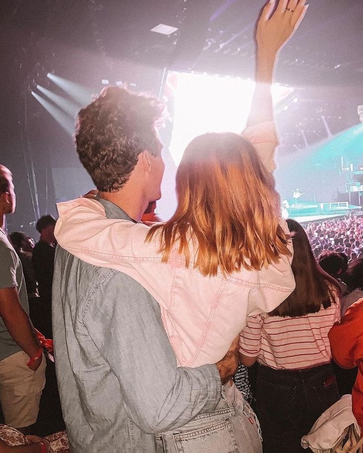 a man and woman are standing in front of a crowd at a concert with their arms raised