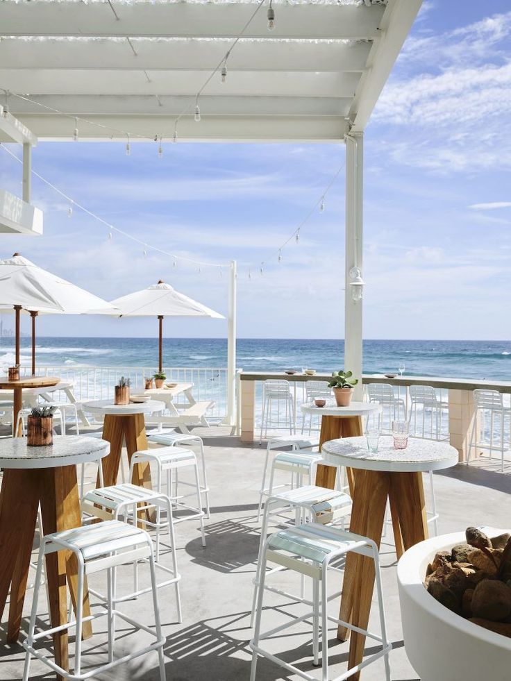 an outdoor dining area overlooking the ocean with white chairs and tables set up under umbrellas