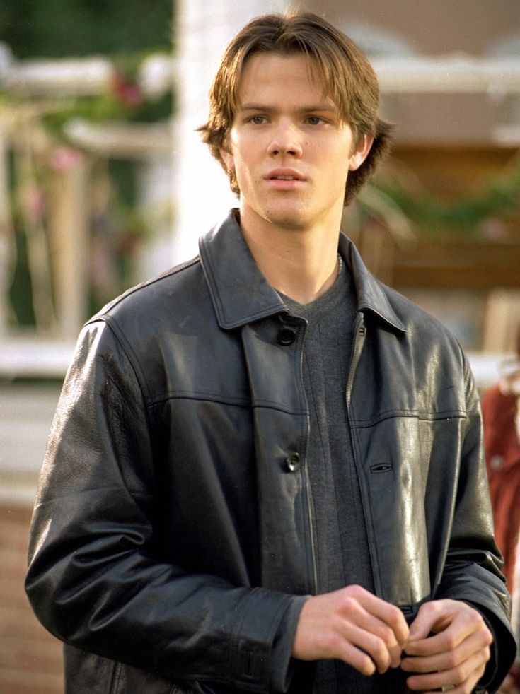 the young man is wearing a black leather jacket and looking off to the side with his hands in his pockets