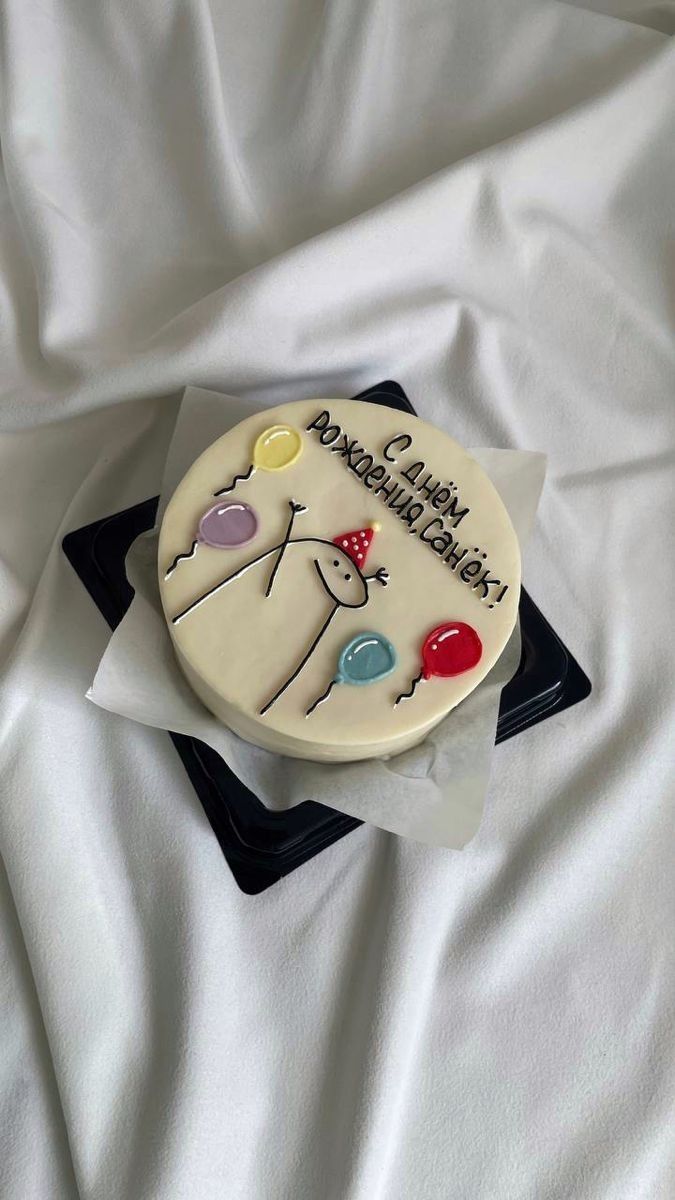 a birthday cake with balloons on it sitting on top of a white sheet covered bed