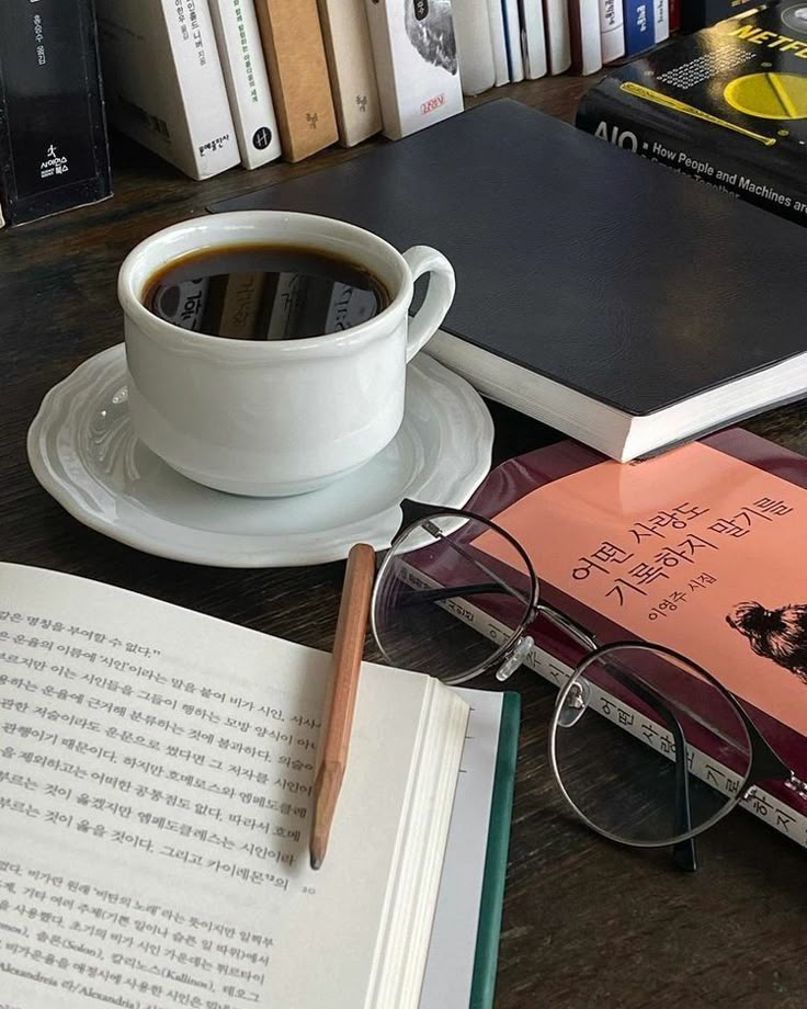 a cup of coffee sitting on top of a table next to an open book and eyeglasses