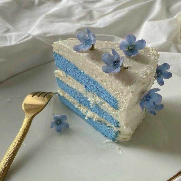 a piece of blue cake with white frosting and flowers on the side next to a fork