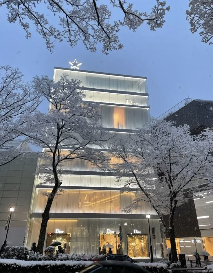 the building is lit up at night with snow on the ground and trees in front