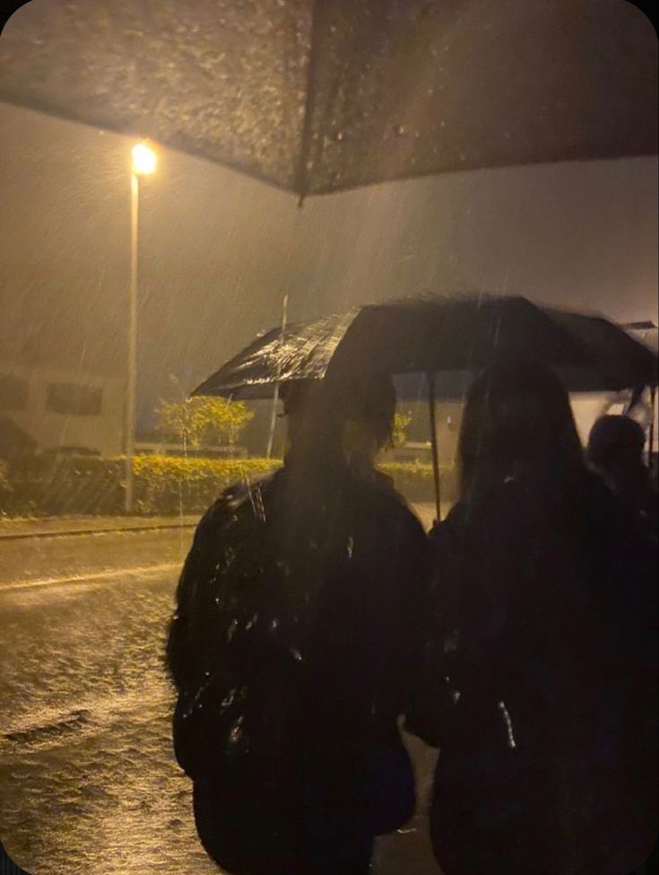 two people standing under an umbrella on a rainy night in the rain with their backs to each other