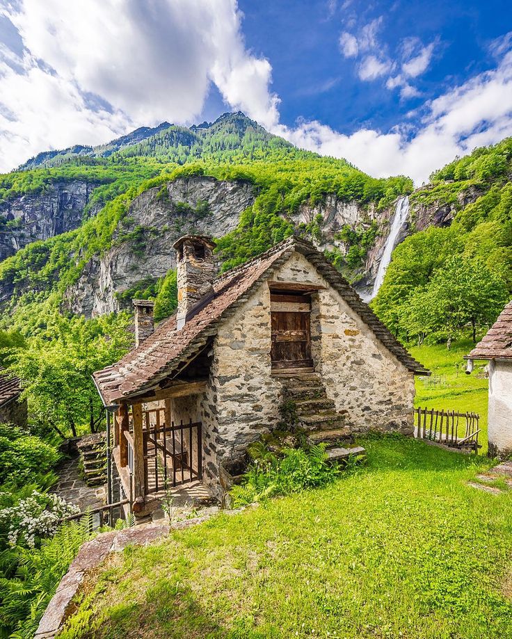 an old stone house in the mountains with a waterfall coming out of it's window