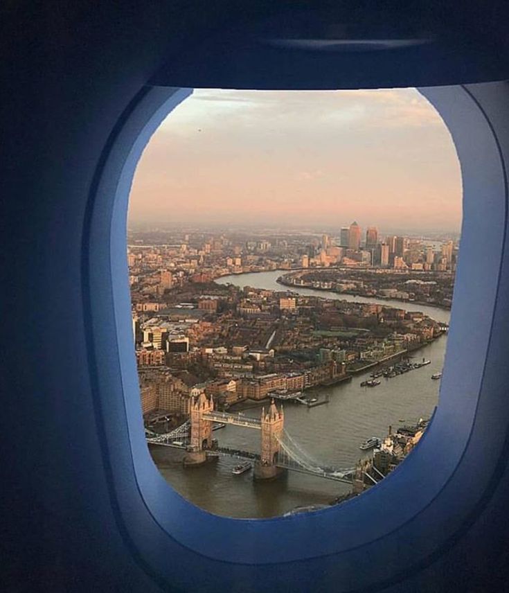 an airplane window with the view of london and tower bridge in the distance as seen from above