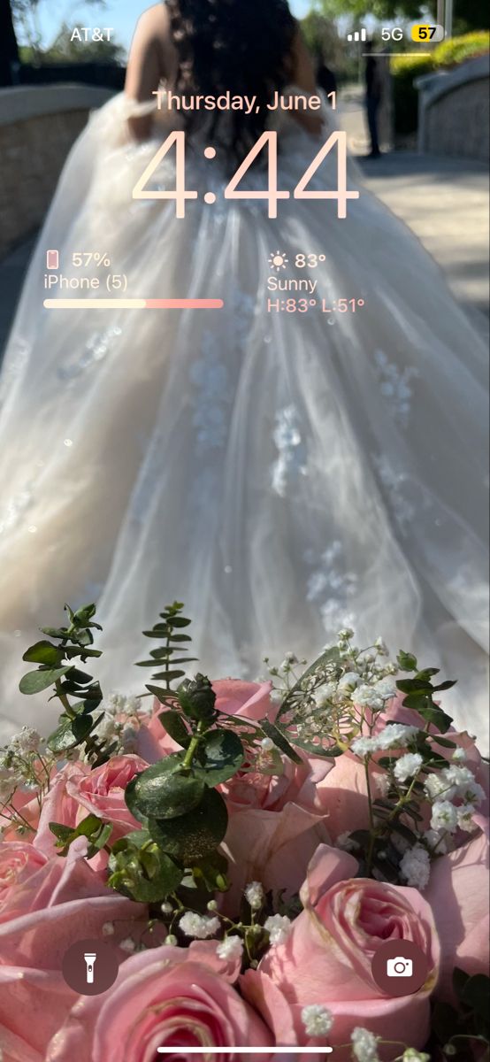 a wedding photo taken on the phone with pink roses and greenery in front of it