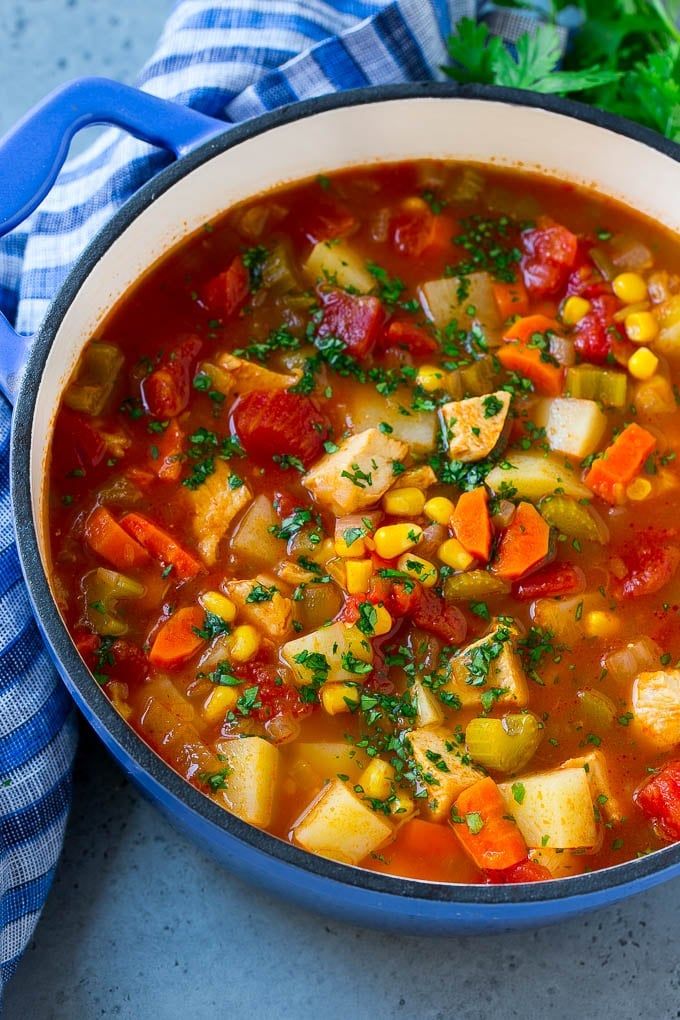 a blue pot filled with vegetable soup and garnished with parsley on the side