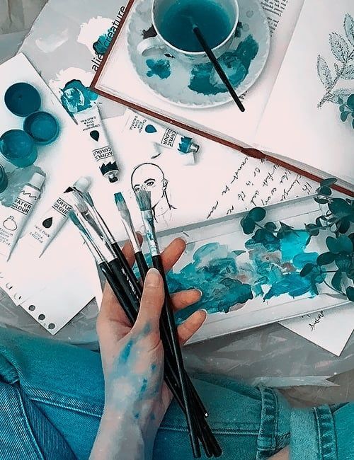 a person holding paint brushes in their hands and painting on paper with watercolors