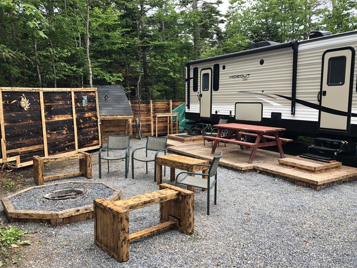 an rv parked in the woods next to some tables and chairs with benches around it