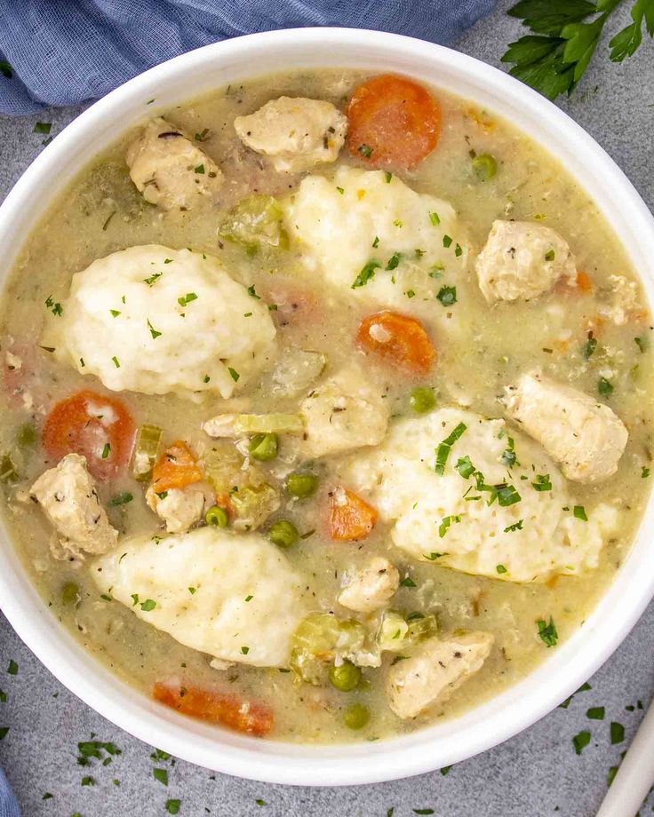 a bowl of chicken and dumpling soup with carrots, celery and parsley