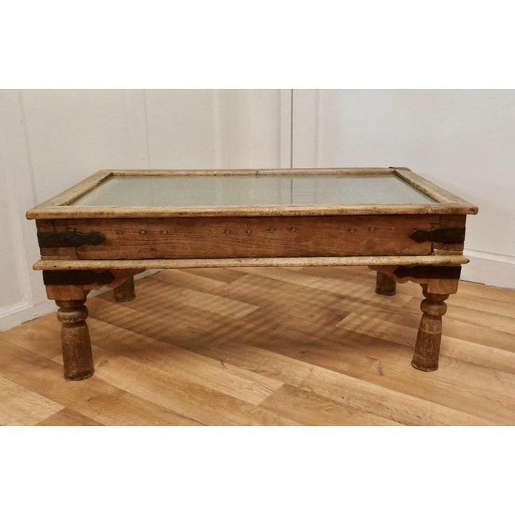 an old coffee table with glass top and wooden legs, in the middle of a room