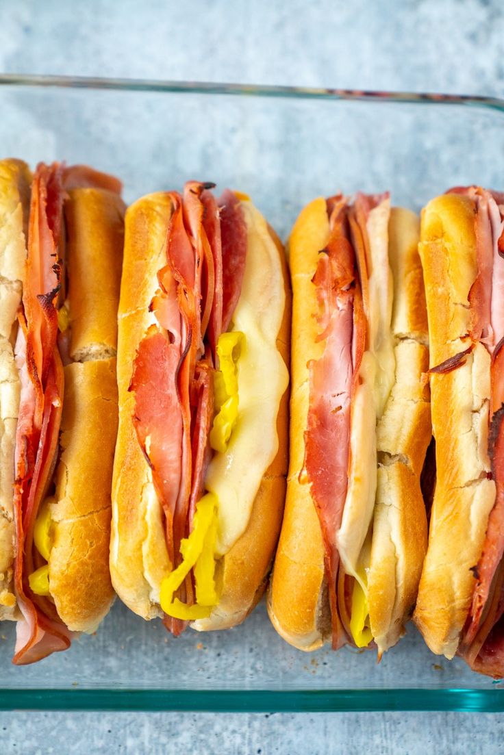 four hotdogs are lined up in a row on a glass tray with mustard and ketchup