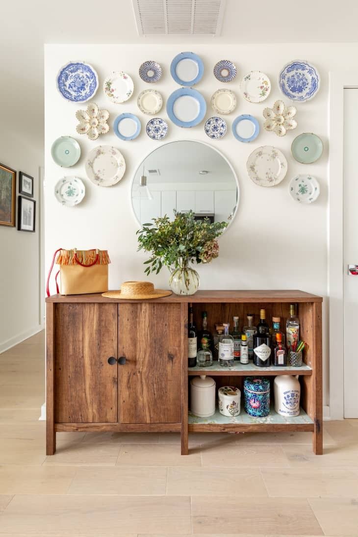 a wooden cabinet sitting under a mirror next to a wall with plates and bowls on it