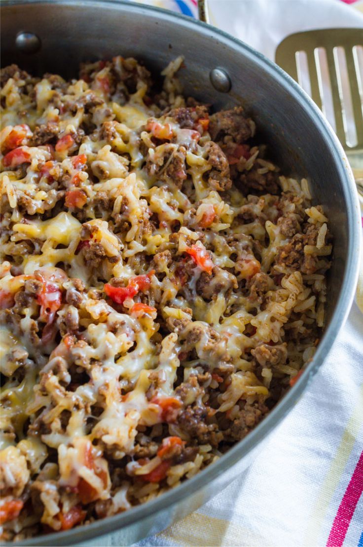 a skillet filled with meat and cheese on top of a striped table cloth next to utensils