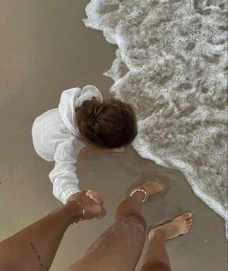 two people standing on the beach with their feet in the sand and one is wearing a white shirt