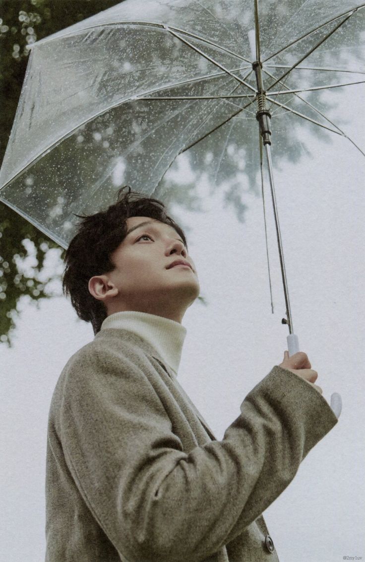 a young man holding an umbrella in the rain while looking up at the treetops