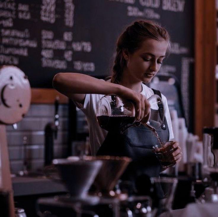 a woman pouring something into a glass in front of a chalkboard