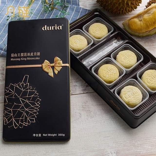 four cookies in a black box on a table with pine cones and other food items