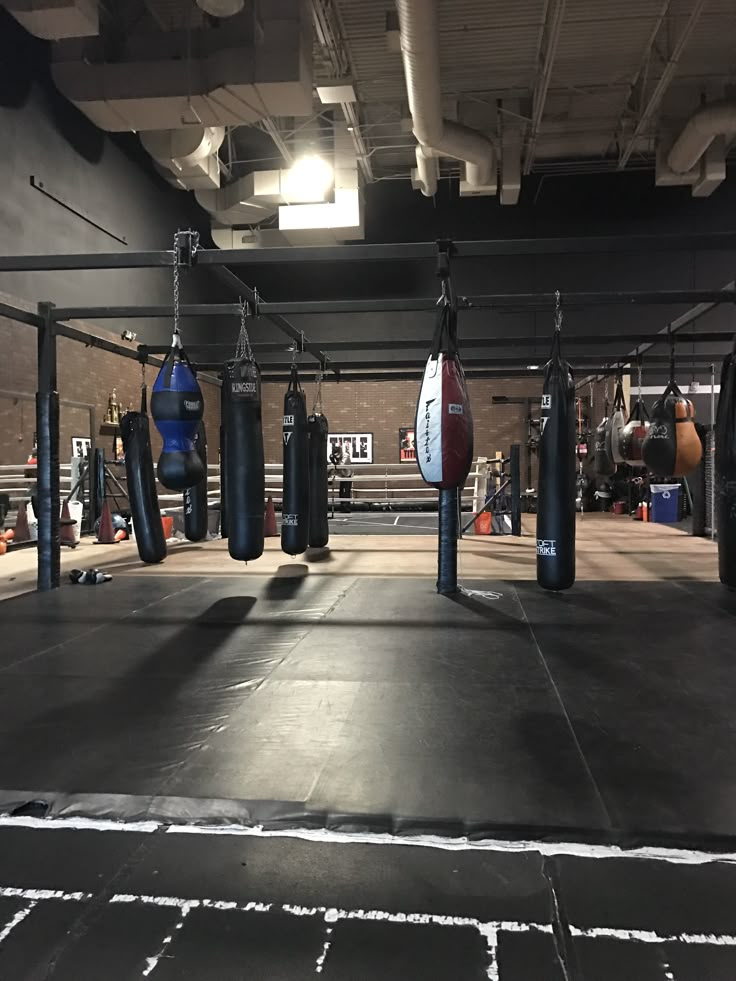 an empty boxing ring with punching gloves hanging from the ceiling and other equipment on the ground