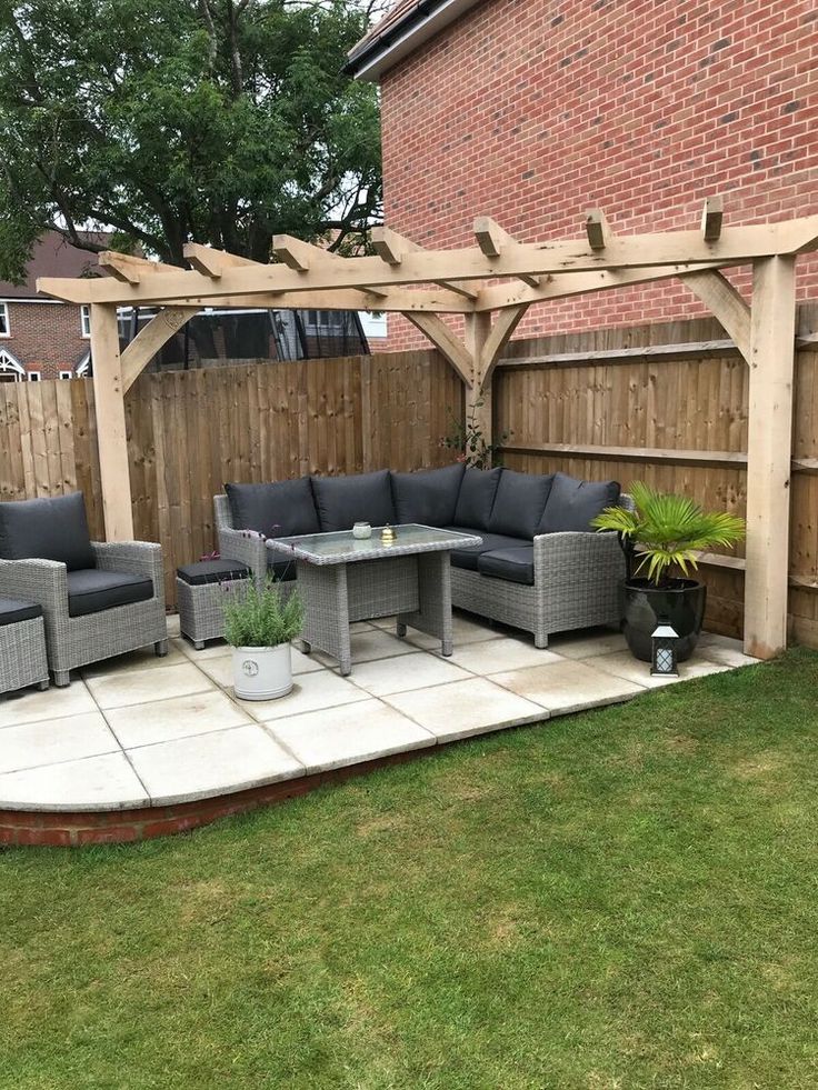 a patio with couches and tables in the grass next to a wooden fenced area