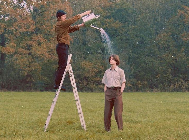 two people are standing on a ladder and one is watering the grass