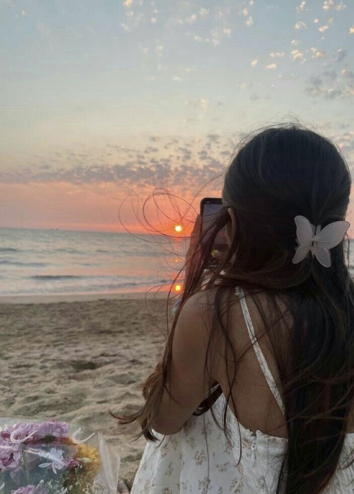 a woman standing on top of a sandy beach next to the ocean with a butterfly in her hair