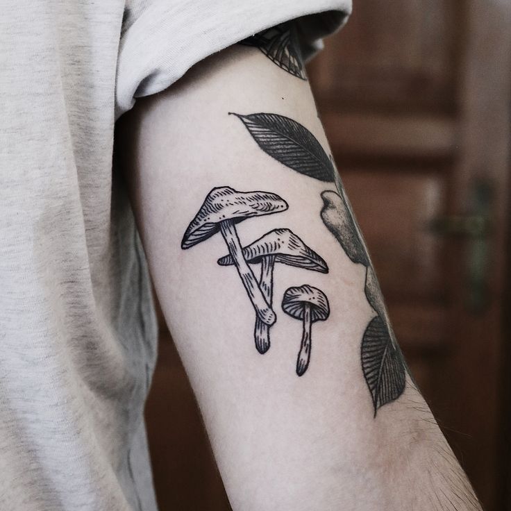 a man's arm with mushrooms and leaves tattooed on the left side of his arm