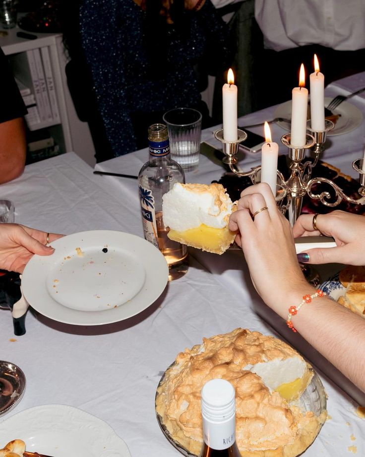 several people are sitting at a table with pies and candles