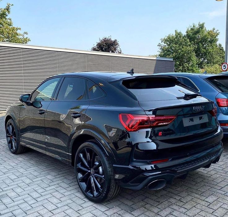 the rear end of a black suv parked in a parking lot next to other cars