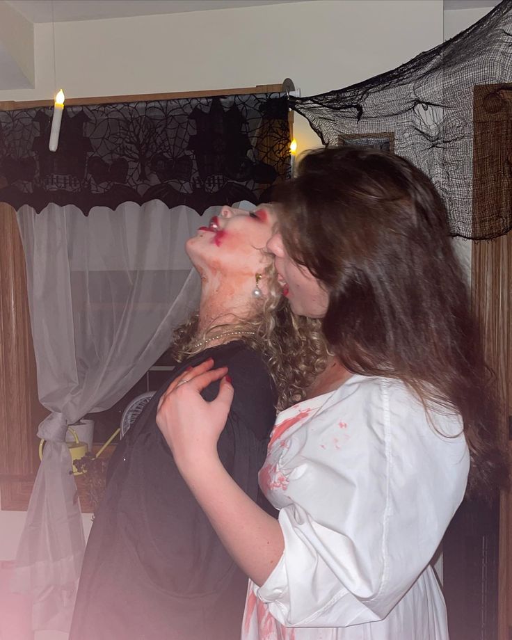 two women are kissing in front of a halloween decoration with lights on the wall behind them