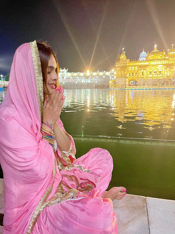 a woman in a pink sari sitting on the edge of a body of water