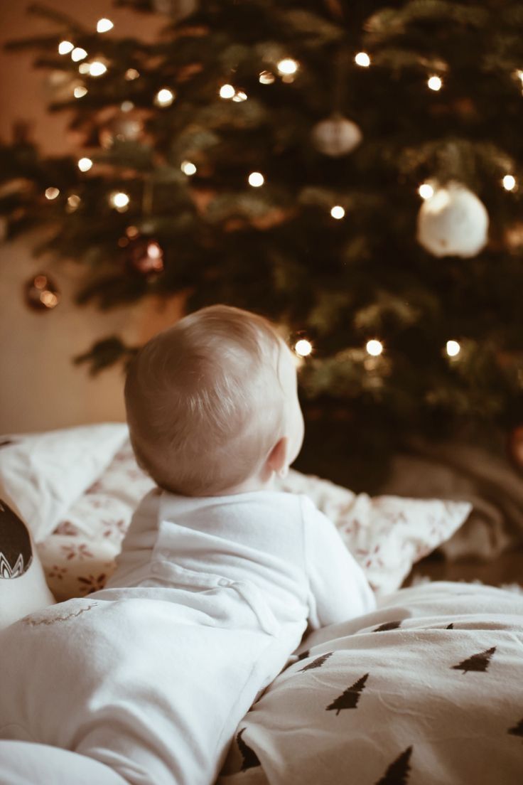 a baby laying on top of a bed next to a christmas tree