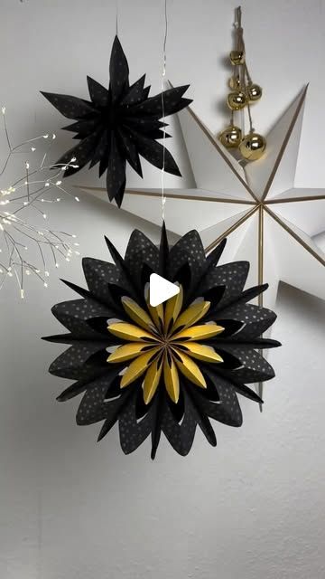 three black and gold paper flowers hanging from the ceiling in a room with white walls