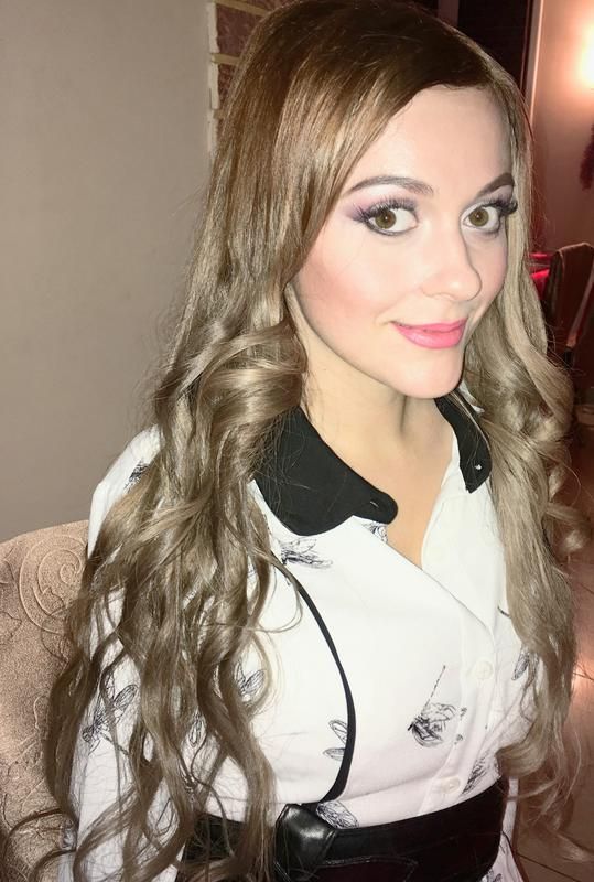 a woman with long hair wearing a white shirt and black belted dress posing for the camera