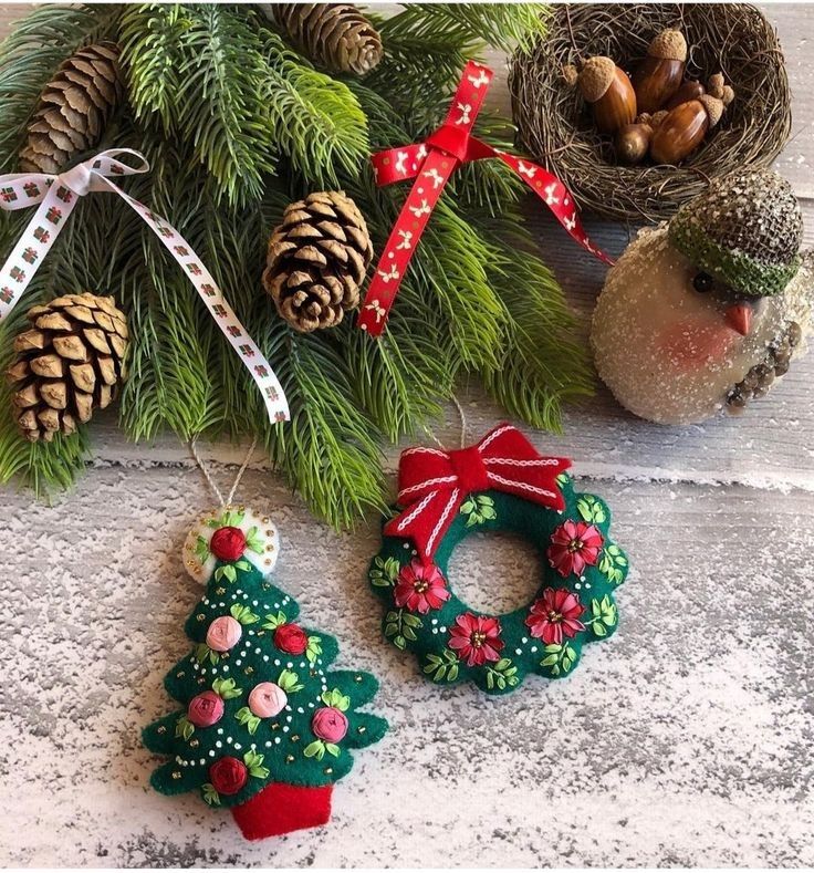 two christmas ornaments are sitting on the ground next to pine cones and other holiday decorations