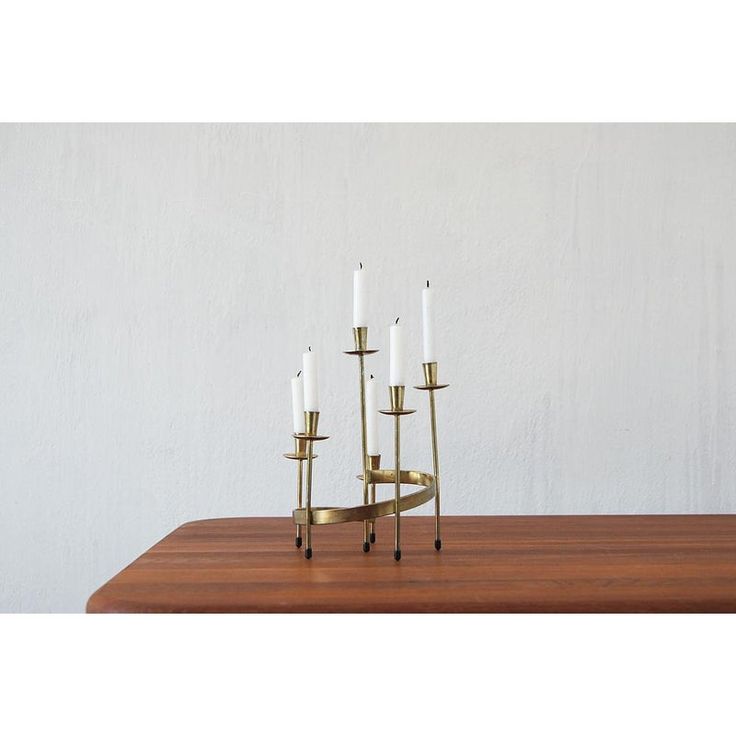 a brass candle holder with five candles on a wooden table in front of a white wall