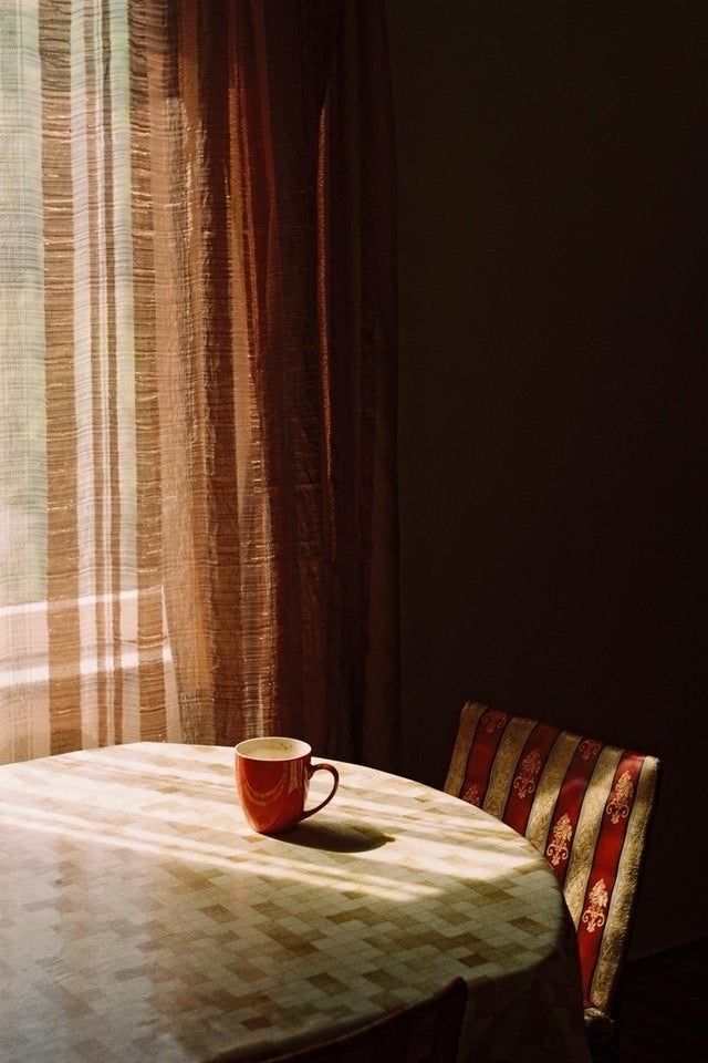 a coffee cup sitting on top of a table next to a window with sheer curtains