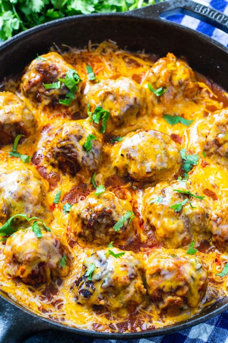 a skillet filled with meatballs covered in cheese and garnished with parsley