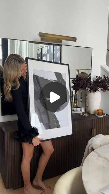 a woman standing in front of a mirror holding up a framed photo with her legs crossed