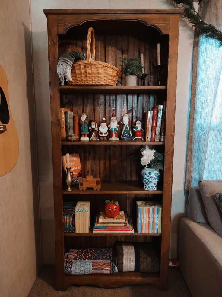 a wooden book shelf filled with books next to a couch and guitar on the wall