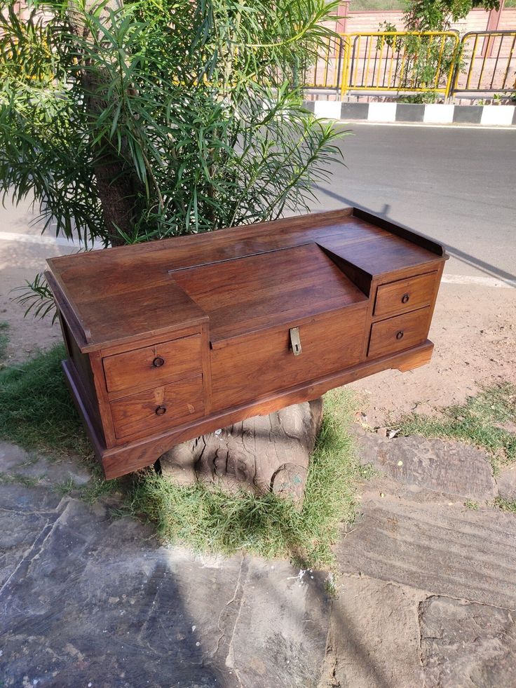 an old wooden desk sitting on the ground next to a tree and grass covered sidewalk