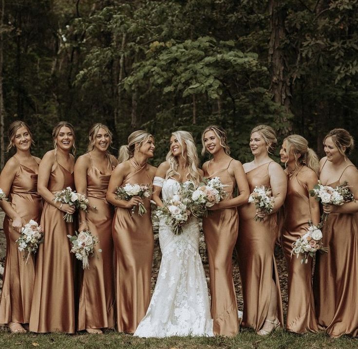 a group of women standing next to each other in front of trees and bushes with bouquets