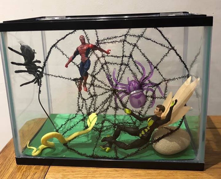 two figurines in a glass case on a wooden table next to a spiderman figure