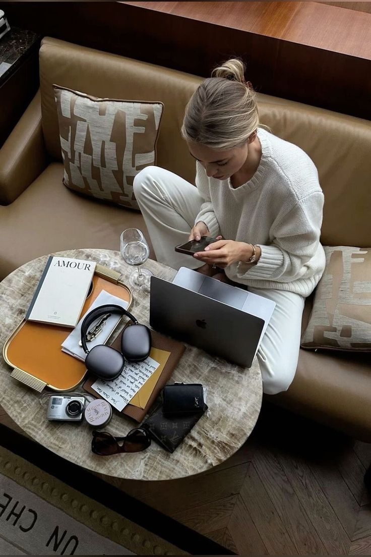 a woman sitting on a couch looking at her cell phone and laptop computer with headphones