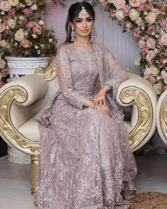 a woman sitting on top of a white chair in front of a flower covered wall