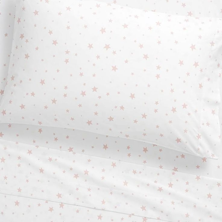 a bed with white sheets and pink stars on the pillowcase, along with two pillows