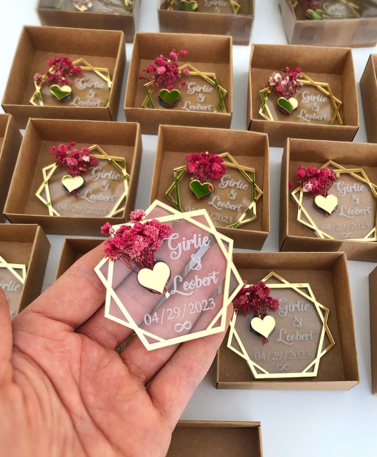 someone is holding their wedding favors in front of many small boxes with flowers and hearts on them