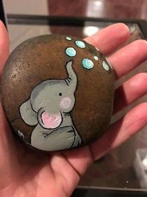 a hand holding a painted rock with an elephant on it's face and bubbles coming out of its trunk