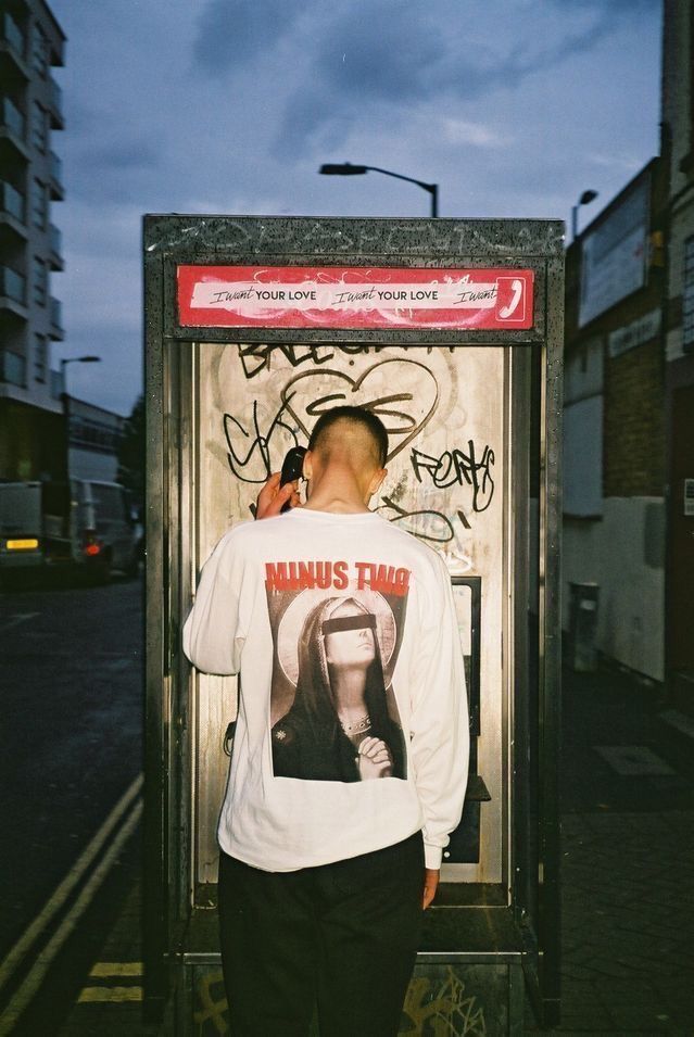 a man standing in front of a phone booth with graffiti on the wall behind him